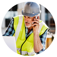 Construction worker on site in hard hat using mobile device and laptop