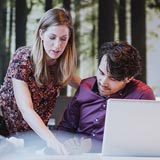 Woman assisting man with project at office table pointing at project