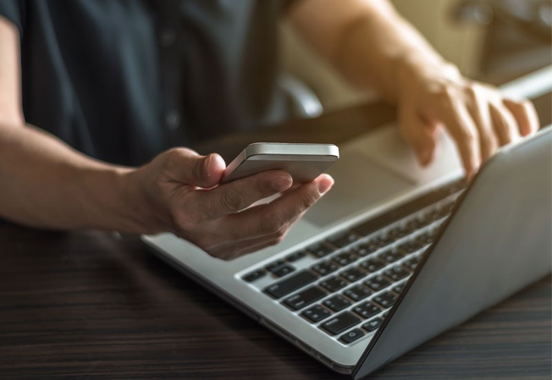Business owner calling remote technical assistance center from smart phone while on notebook computer
