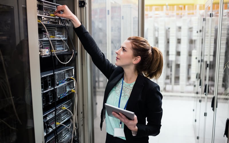 IT professional reaches for cable in data center with tablet in hand